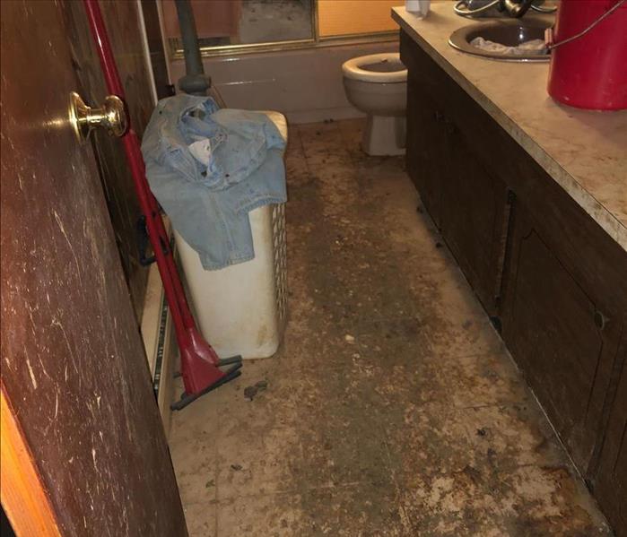 A bathroom with the floor and laundry basket covered in debris