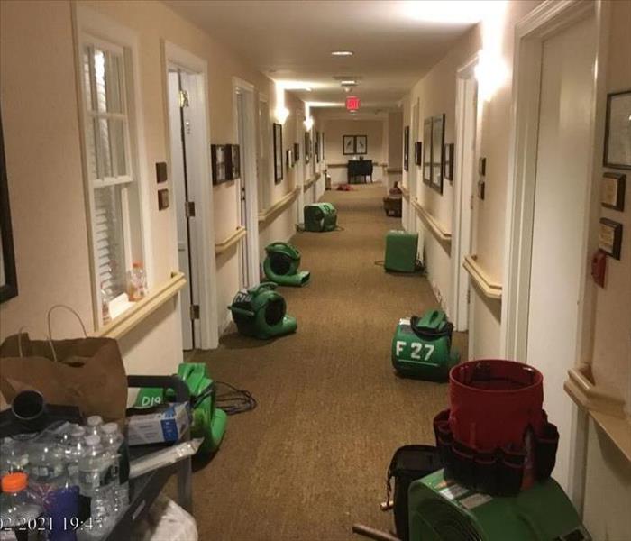 Multiple air movers operating down a long carpeted hallway with removed base molding